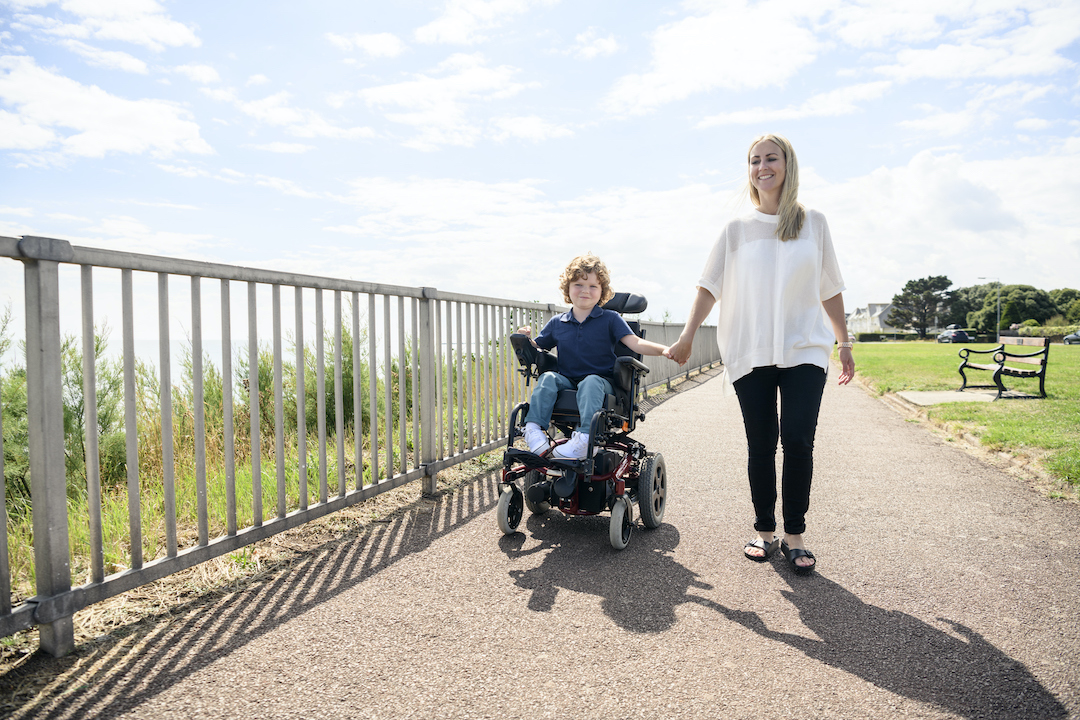 Jeune garçon handicapé en fauteuil roulant accompagné par sa maman
