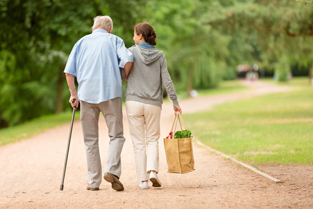 Jeune femme portant les courses d'un monsieur âgé, en le prenant par le bras