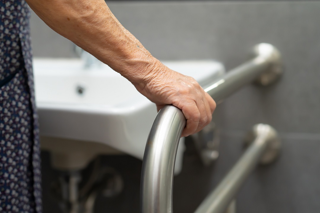 main d'une personne âgée tenant une rampe de douche, à côté du lavabo de salle de bain.
