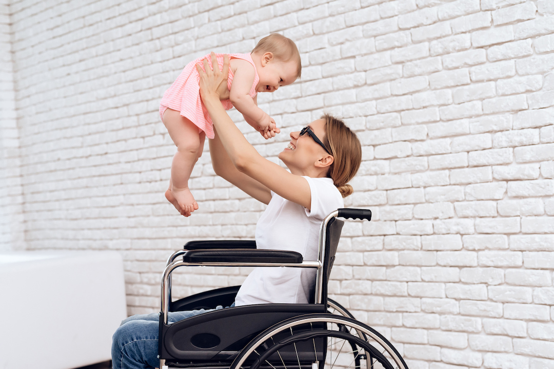 Maman handicapée dans un fauteuil roulant tenant son bébé dans les bras.